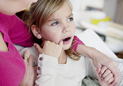 Little girl in dental chair pointing to tooth